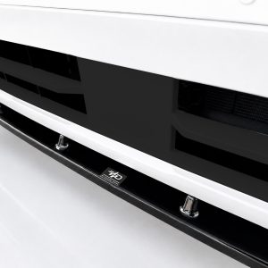 Close-up of a white car front bumper with a black grille and chrome lower lip, a small emblem visible