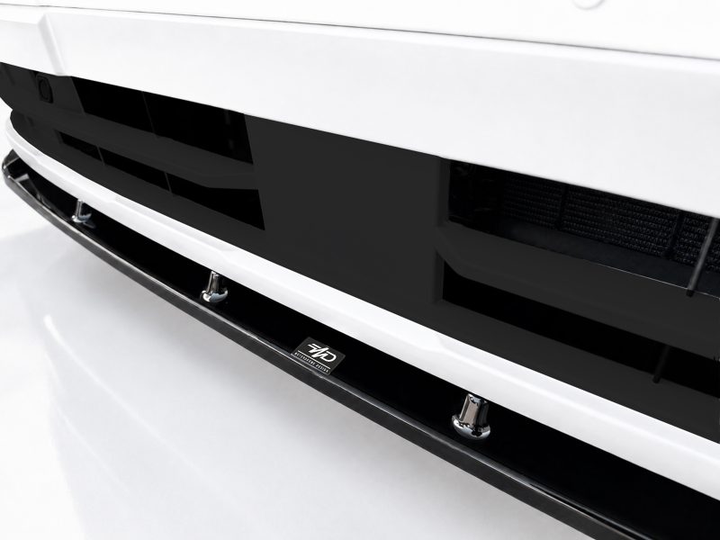 Close-up of a white car front bumper with a black grille and chrome lower lip, a small emblem visible