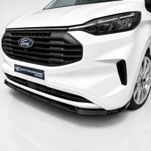 Front-left angle of a white Ford van with a large black grille and badge, displaying a 'MOTORODOME DESIGN' plate at the bumper edge, showroom backdrop