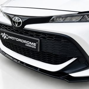 Close-up of a white car's front end with a black honeycomb grille and a license plate reading MOTORDROME DESIGN.