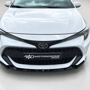 Front view of a white Toyota with a black honeycomb grille and Toyota emblem, displaying Motordrome Design plate.