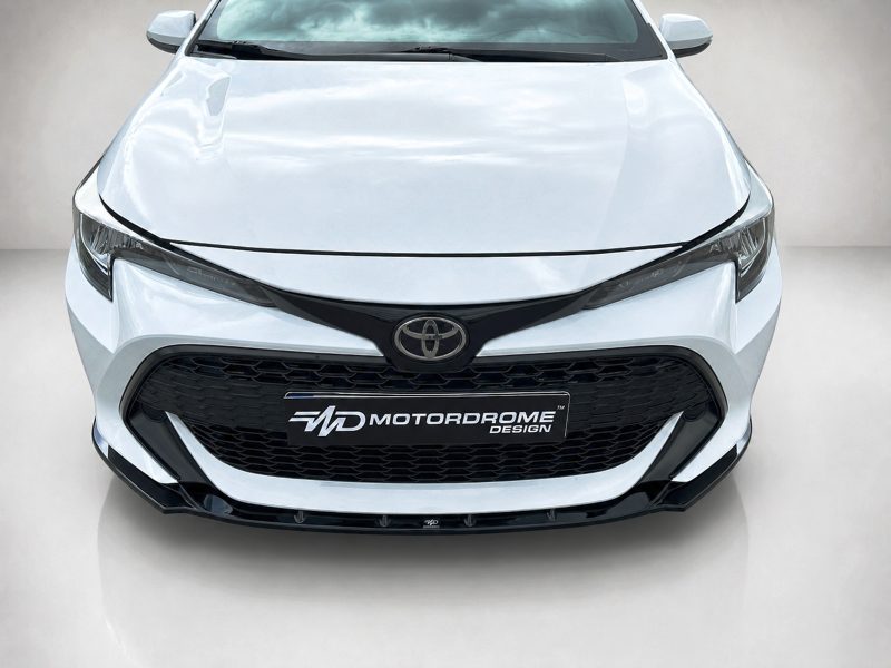 Front view of a white Toyota with a black honeycomb grille and Toyota emblem, displaying Motordrome Design plate.
