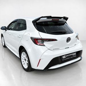 Rear three-quarter view of a white Toyota hatchback with a prominent spoiler in a bright studio setting.