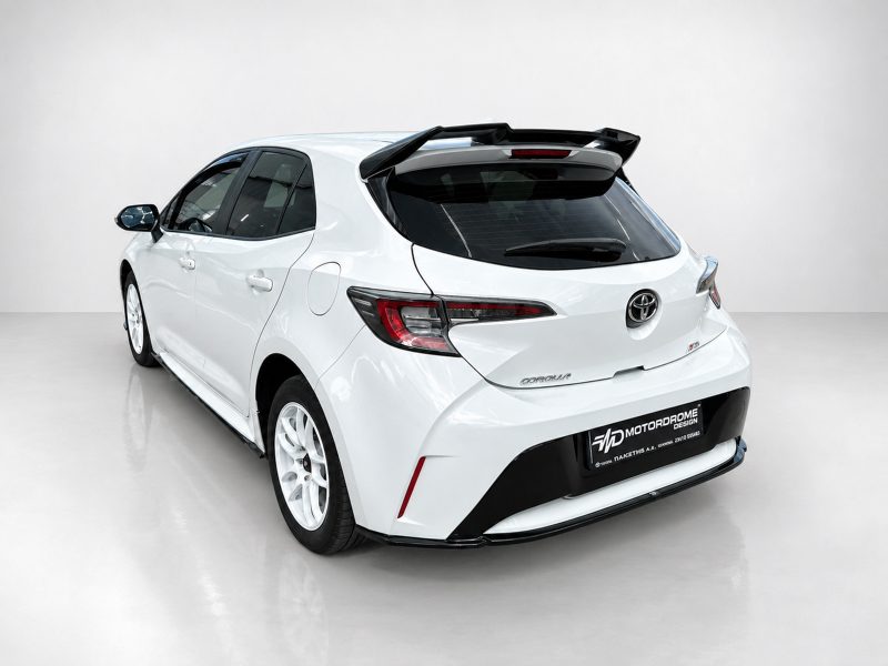 Rear three-quarter view of a white Toyota hatchback with a prominent spoiler in a bright studio setting.