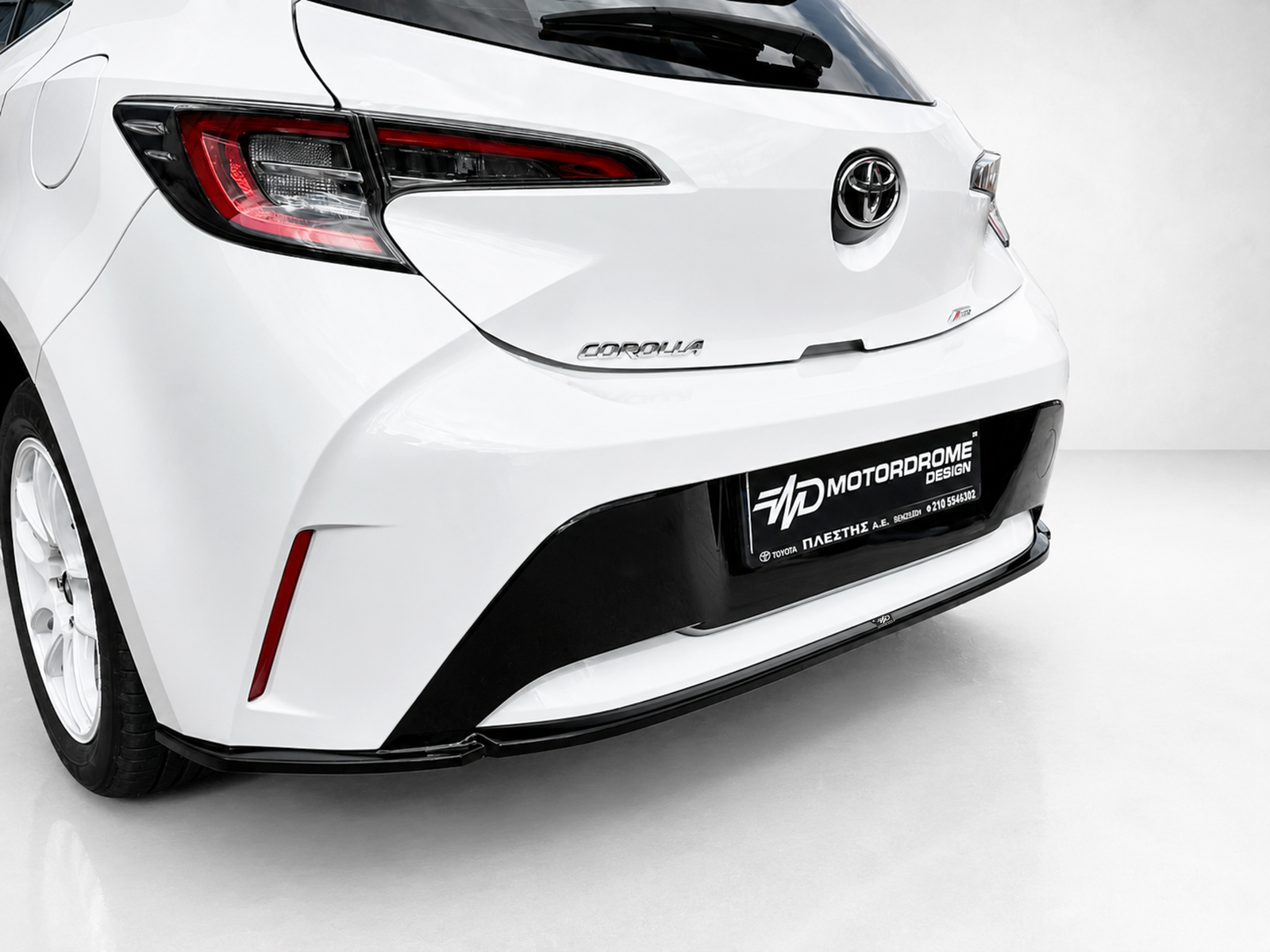 K201-003_2jpg - OPSHOLDERS White Toyota Corolla rear view with prominent taillights and a black lower bumper, license plate area labeled Motordrome Design.