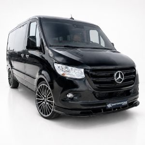Front three-quarter view of a glossy black Mercedes-Benz van with aftermarket multi-spoke wheels, set against a white studio background.