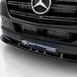 Close-up of the front of a glossy black car showing the grille, Mercedes emblem, and a MotorDome Design plate nearby.