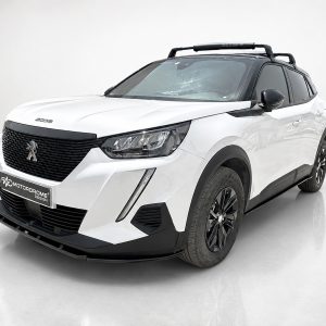 Front three-quarter view of a white Peugeot 5008 SUV with a black grille, roof rack, and dark windows in a studio setting.