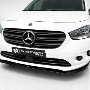 Front view of a white Mercedes van with a black grille and prominent emblem, featuring a MotorDome Design plate on the bumper.