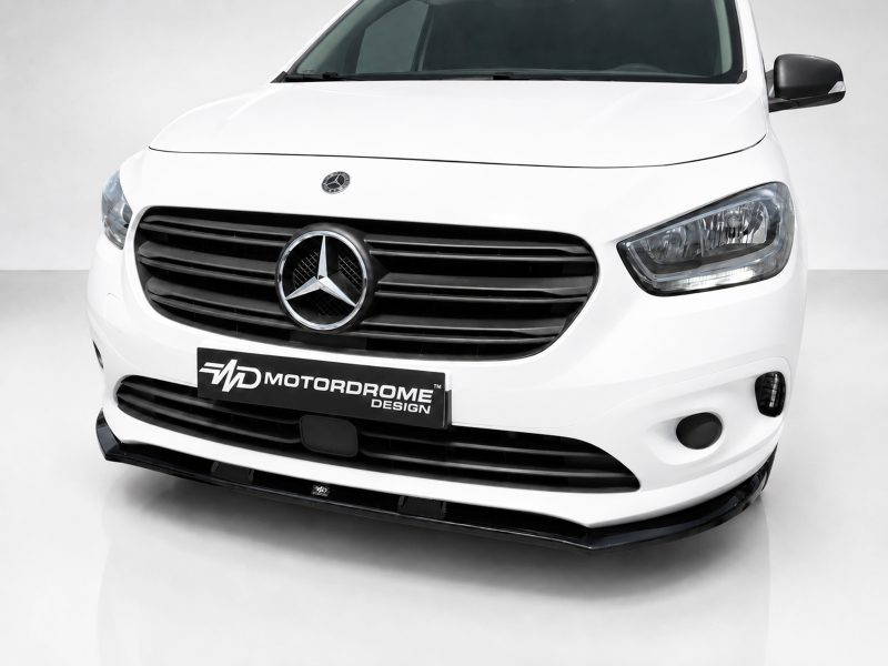 Front view of a white Mercedes van with a black grille and prominent emblem, featuring a MotorDome Design plate on the bumper.