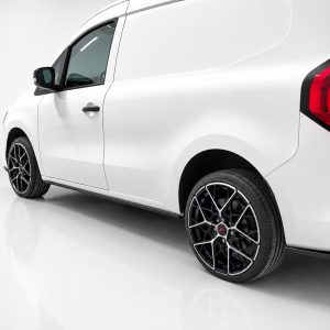 White cargo van shown from a rear-side angle with black multi-spoke alloy wheels in a studio setting