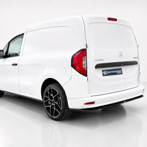 White cargo van shown from rear-left in a studio, featuring black bumper and angular alloy wheels with a Motordrome Design badge on the rear door.