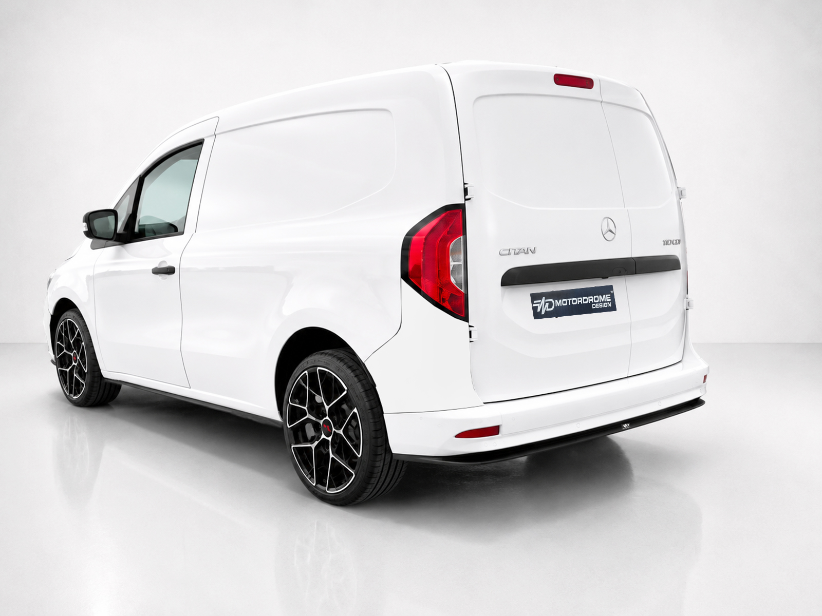 K204-003_1jpg - OPSHOLDERS White cargo van shown from rear-left in a studio, featuring black bumper and angular alloy wheels with a Motordrome Design badge on the rear door.