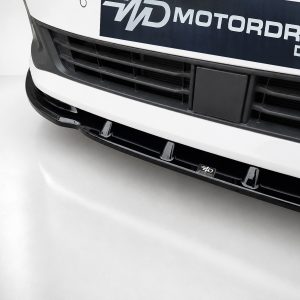 Close-up of a white car's front bumper and grille with a small black license plate area and WD Motors Design branding plate visible.