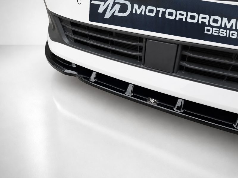 Close-up of a white car's front bumper and grille with a small black license plate area and WD Motors Design branding plate visible.