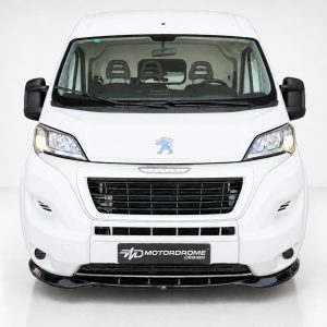 Front view of a white Peugeot van in a studio setting, showing the grille, headlights, and Peugeot emblem on the hood.
