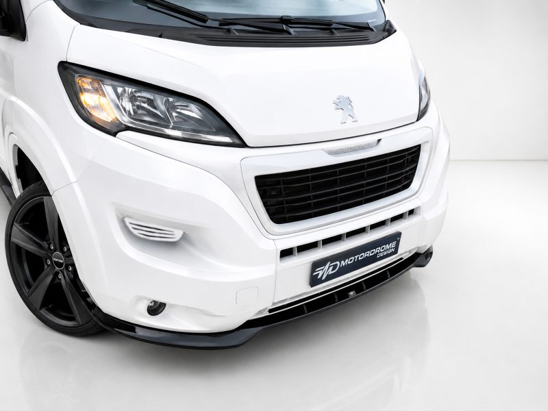Front-left view of a white Peugeot van, displaying the headlight, emblem, and large grille