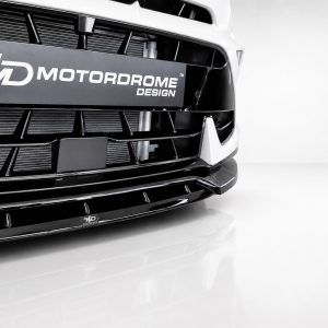 Close-up of the front bumper and grille of a white car with a black Motordrome Design plate across the grille area.