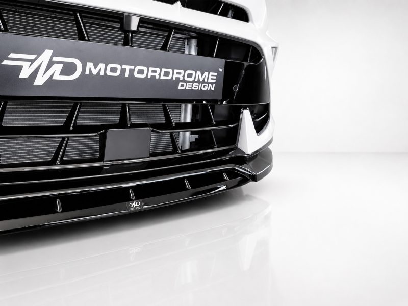 Close-up of the front bumper and grille of a white car with a black Motordrome Design plate across the grille area.