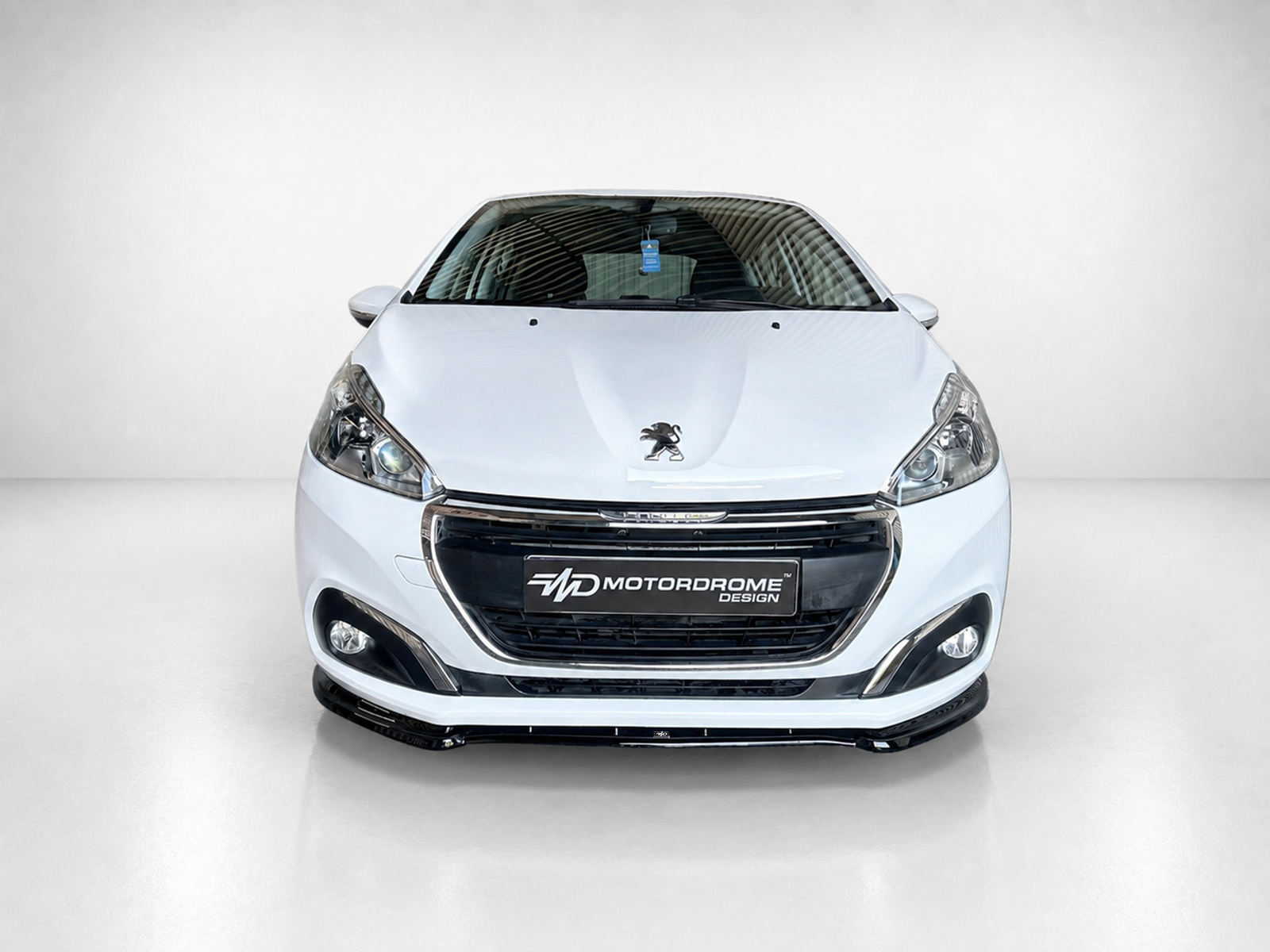 K209-001_1jpg - OPSHOLDERS Front view of a white Peugeot car in a studio setting, showing the grille and badge with a Motordrome Design plate on the front bumper
