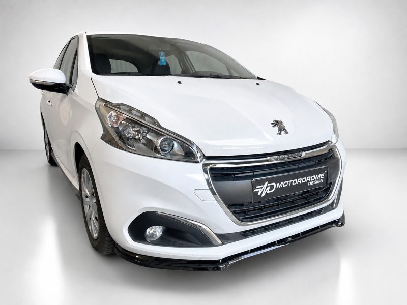 K209-001_3jpg - OPSHOLDERS White Peugeot hatchback photographed in a studio, front three-quarter view showing the grille and emblem, with a MotorDrome Design plate on the bumper.