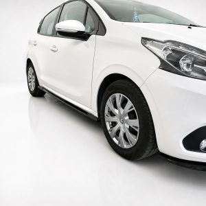White car viewed from a front-right angle in a bright studio setting, showing its headlight and alloy wheel.