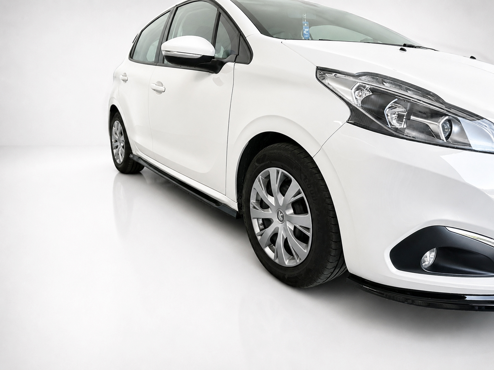 K209-002_1jpg - OPSHOLDERS White car viewed from a front-right angle in a bright studio setting, showing its headlight and alloy wheel.