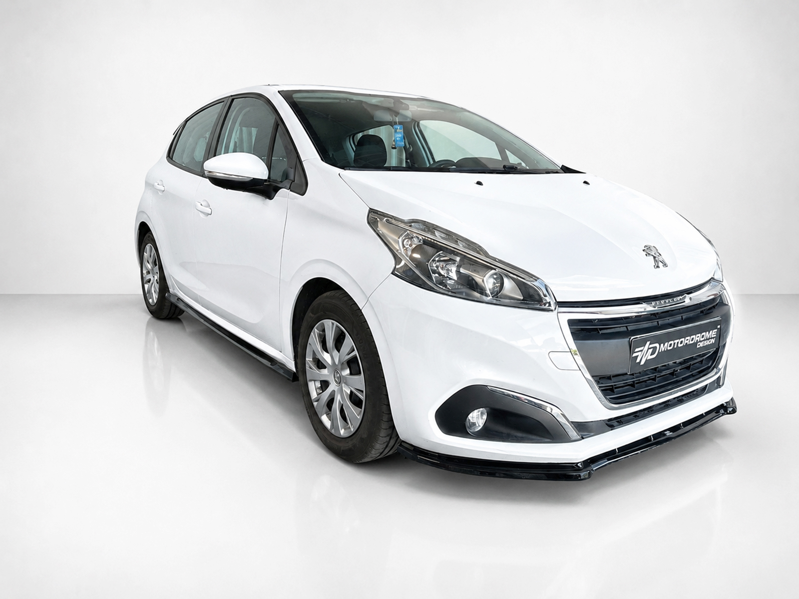 K209-002_2jpg - OPSHOLDERS White Peugeot hatchback shown at a three-quarter angle in a bright studio setting with a glossy floor surface.
