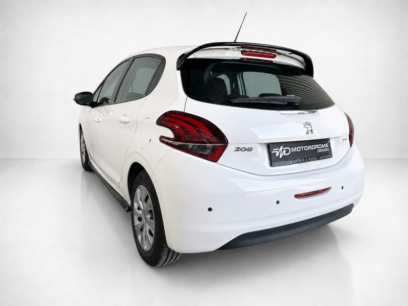 K209-002_4jpg - OPSHOLDERS White Peugeot 208 hatchback seen from the rear-left angle with a roof spoiler and red taillights in a bright studio setting, license plate reading MOTORDROME DESIGN.