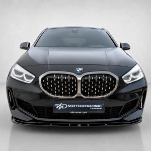 Front view of a sleek black BMW with a distinctive kidney grille, headlights on, set against a neutral backdrop.
