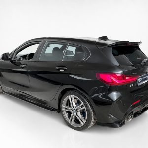 Rear three-quarter view of a glossy black BMW hatchback in a white studio setting, showcasing large alloy wheels and curved body lines.