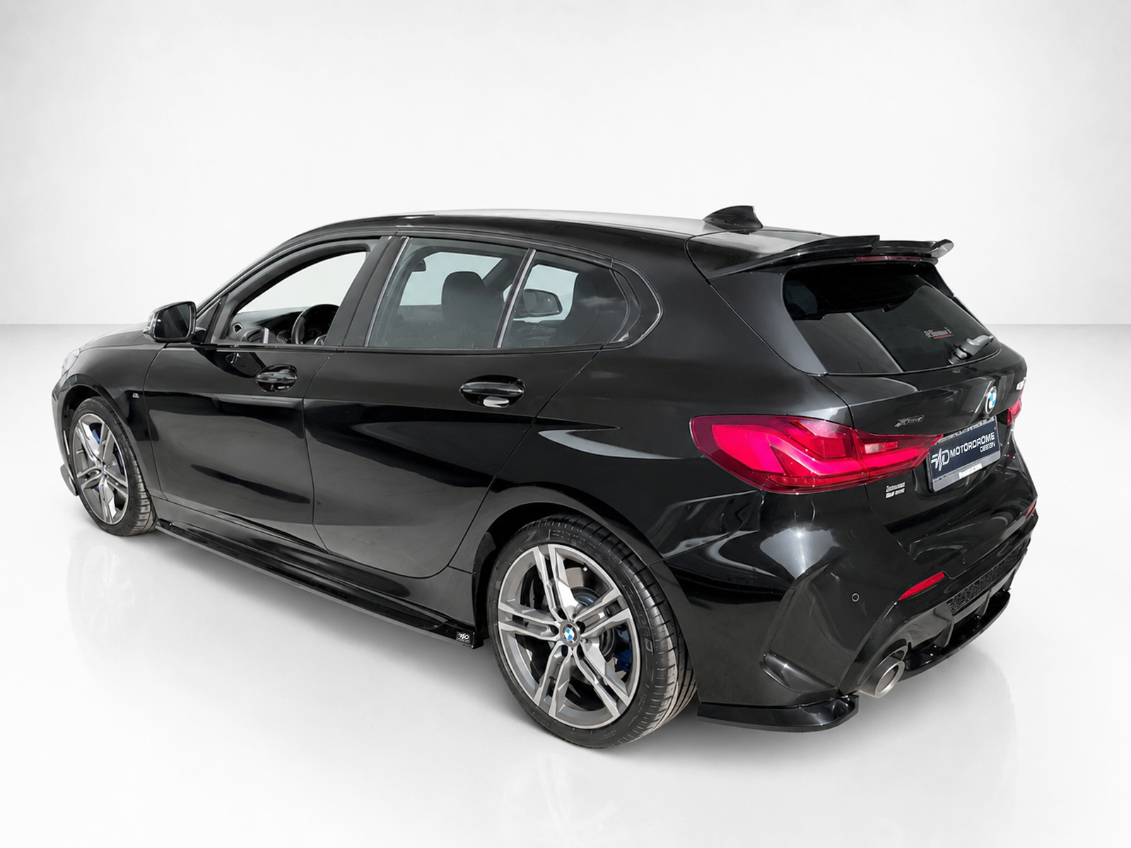 K210-002_1jpg - OPSHOLDERS Rear three-quarter view of a glossy black BMW hatchback in a white studio setting, showcasing large alloy wheels and curved body lines.