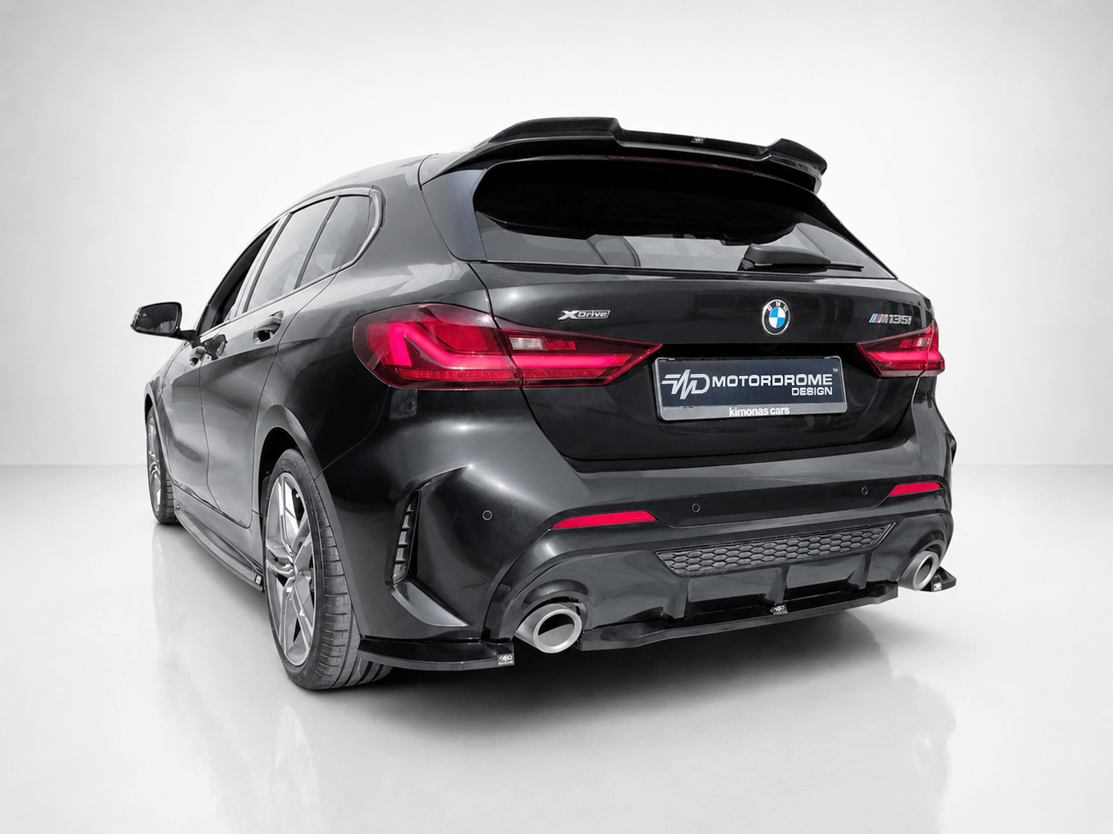 K210-003_1jpg - OPSHOLDERS Rear view of a black BMW M135i xDrive hatchback with red taillights and a Motordrome Design plate, in a white studio setting.