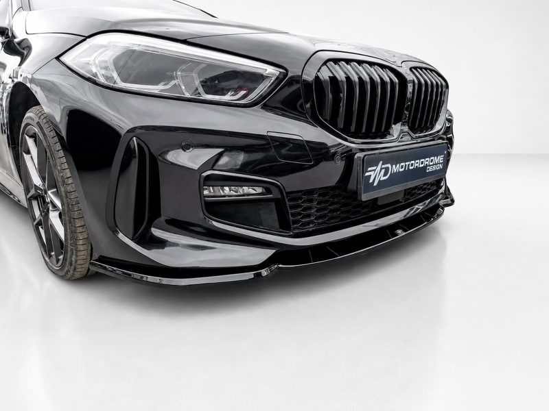 Close-up of a glossy black car front with prominent kidney grille and headlight, featuring a Motordrome Design plate.