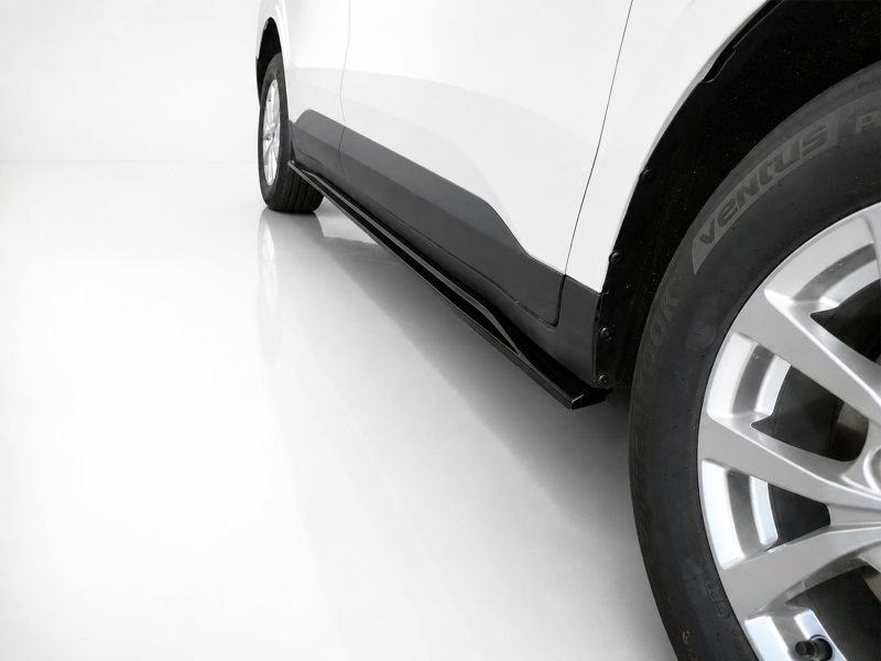 Close-up of a white car's side with a black running board/side step and a visible alloy wheel on the right side