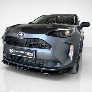 Front-left close-up of a dark gray Toyota with a large grille and a Motordrome Design license plate in a studio setting.