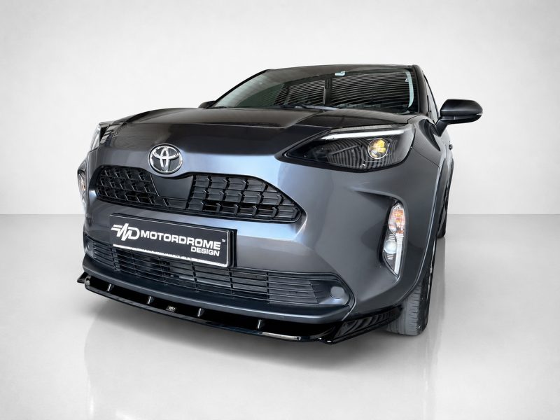 Front-left close-up of a dark gray Toyota with a large grille and a Motordrome Design license plate in a studio setting.