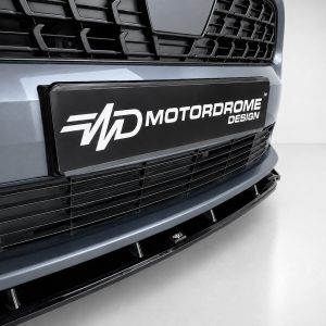Close-up of a car front showing a black plate badge reading MOTORDROME DESIGN on the bumper edge.