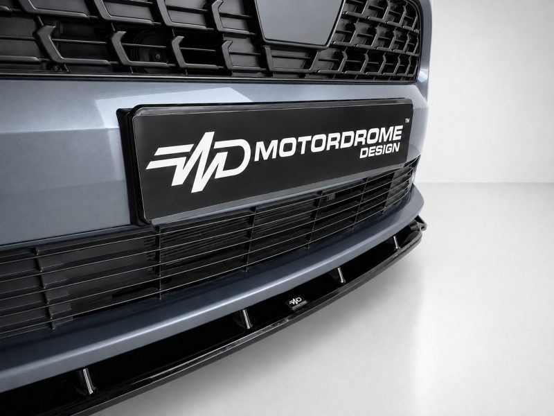 Close-up of a car front showing a black plate badge reading MOTORDROME DESIGN on the bumper edge.