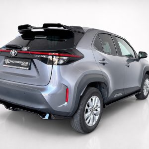 Rear three-quarter view of a silver Toyota Yaris Cross in a studio setting, showing the back and right side with a dealership plate to the rear.