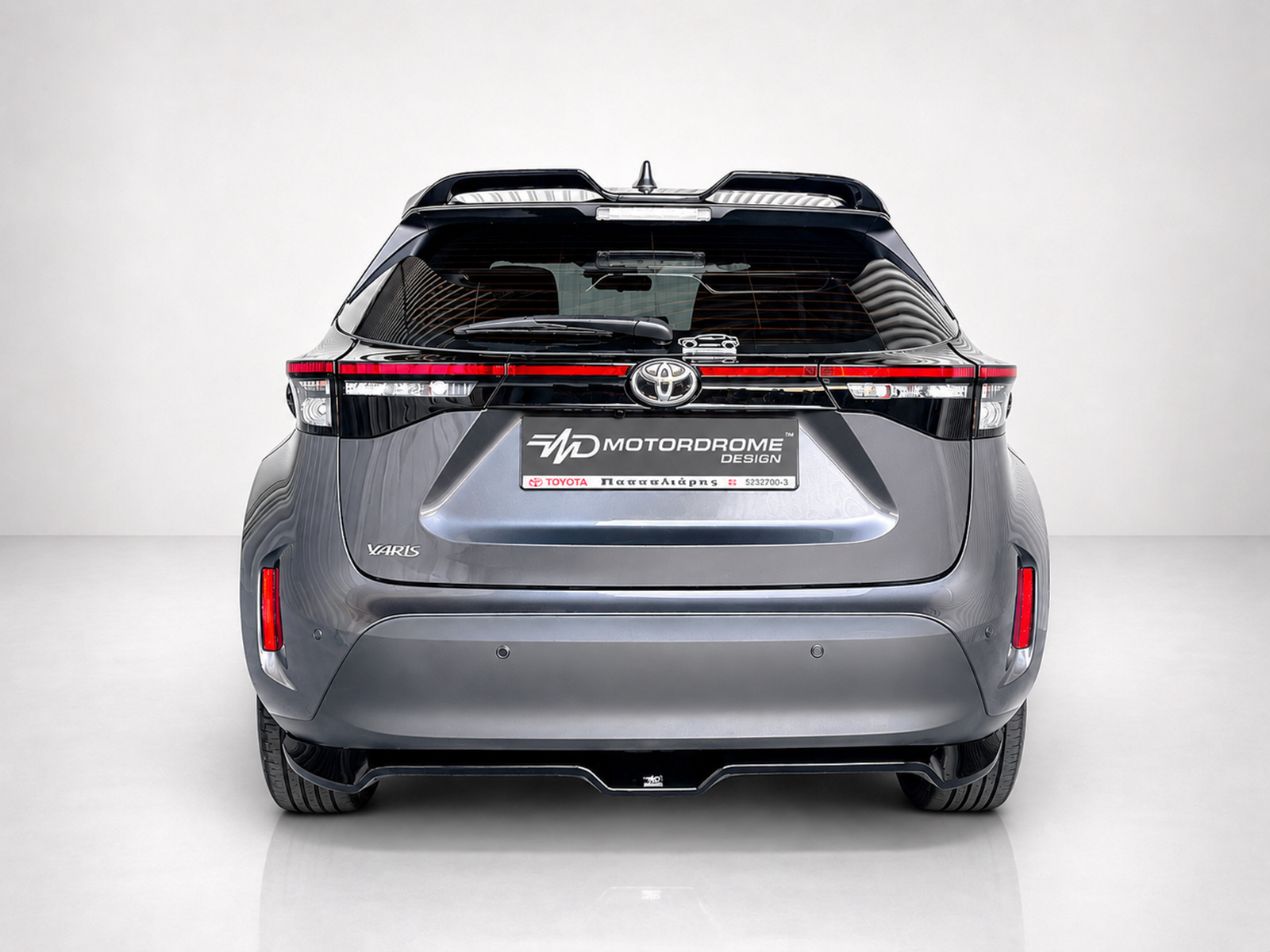 K213-003_1jpg - OPSHOLDERS Rear view of a silver Toyota Yaris hatchback in a studio, showing the taillights, rear window, and branded license plate area.