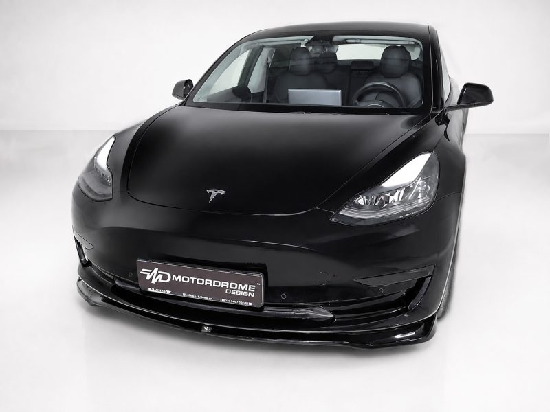 K214-001_3jpg - OPSHOLDERS Front three-quarter view of a black Tesla electric car in a studio setting, showcasing the glossy paint and distinctive headlights.
