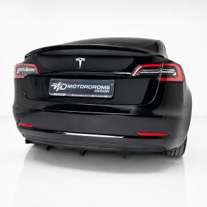 Rear view of a glossy black electric car, showing the Tesla logo and a Motordrome Design plate on the trunk lid.