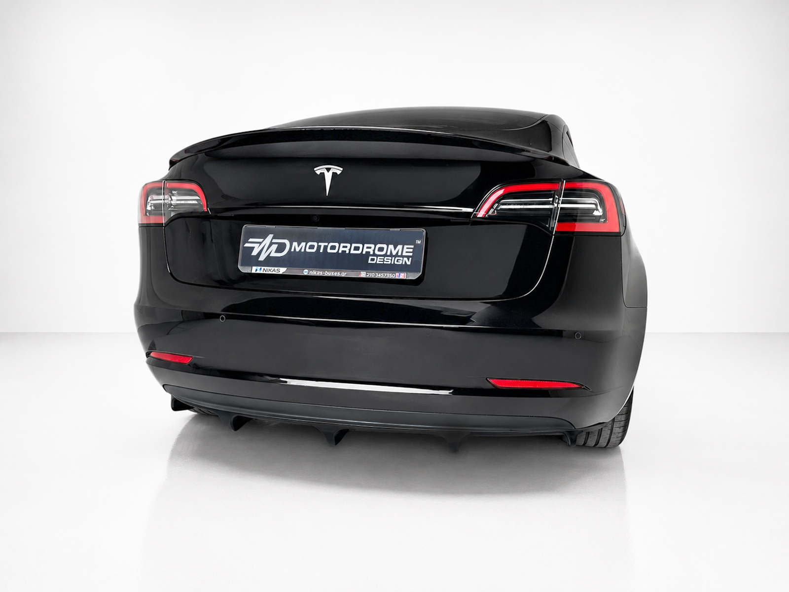 K214-004_1jpg - OPSHOLDERS Rear view of a glossy black electric car, showing the Tesla logo and a Motordrome Design plate on the trunk lid.