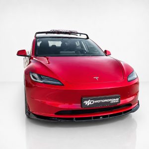 Red Tesla sports car front view with roof rack and visible Tesla emblem, on a white studio backdrop (Motordrome Design plate).