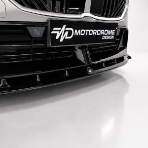Close-up of a car's black front bumper and grille with a MOTORDROME DESIGN license plate captioned plate in the center.