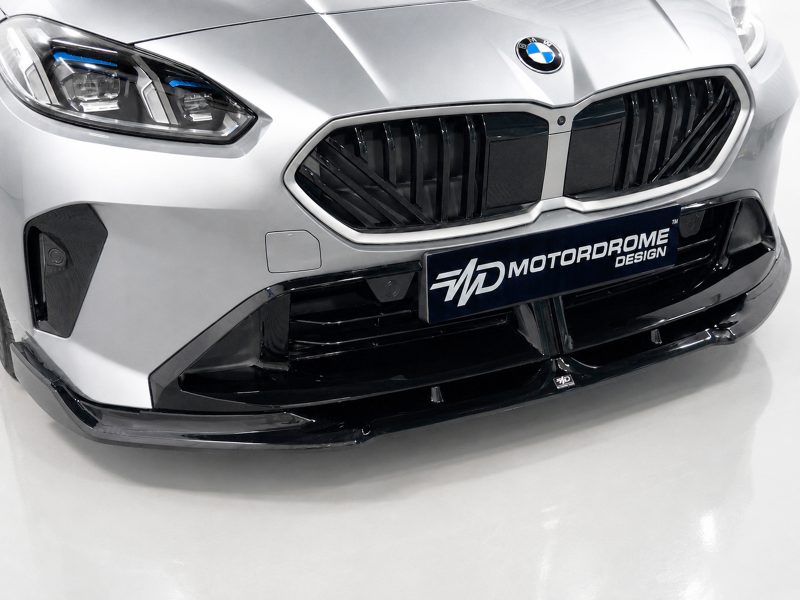Close-up of a silver BMW car front showing the prominent black kidney grille, headlight, and a MOTORDROME DESIGN plate below the grille.