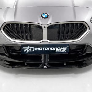 Front view of a silver BMW with a large black kidney grille and a Motordrome Design plate on the bumper.