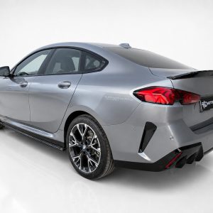 Rear three-quarter view of a silver BMW sedan with large alloy wheels and carbon-fiber rear spoiler in a studio setting.