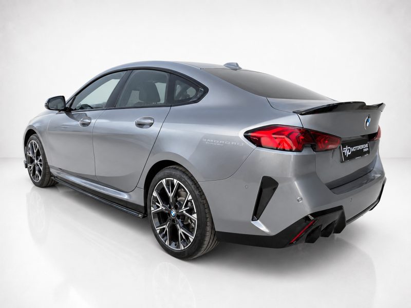 Rear three-quarter view of a silver BMW sedan with large alloy wheels and carbon-fiber rear spoiler in a studio setting.